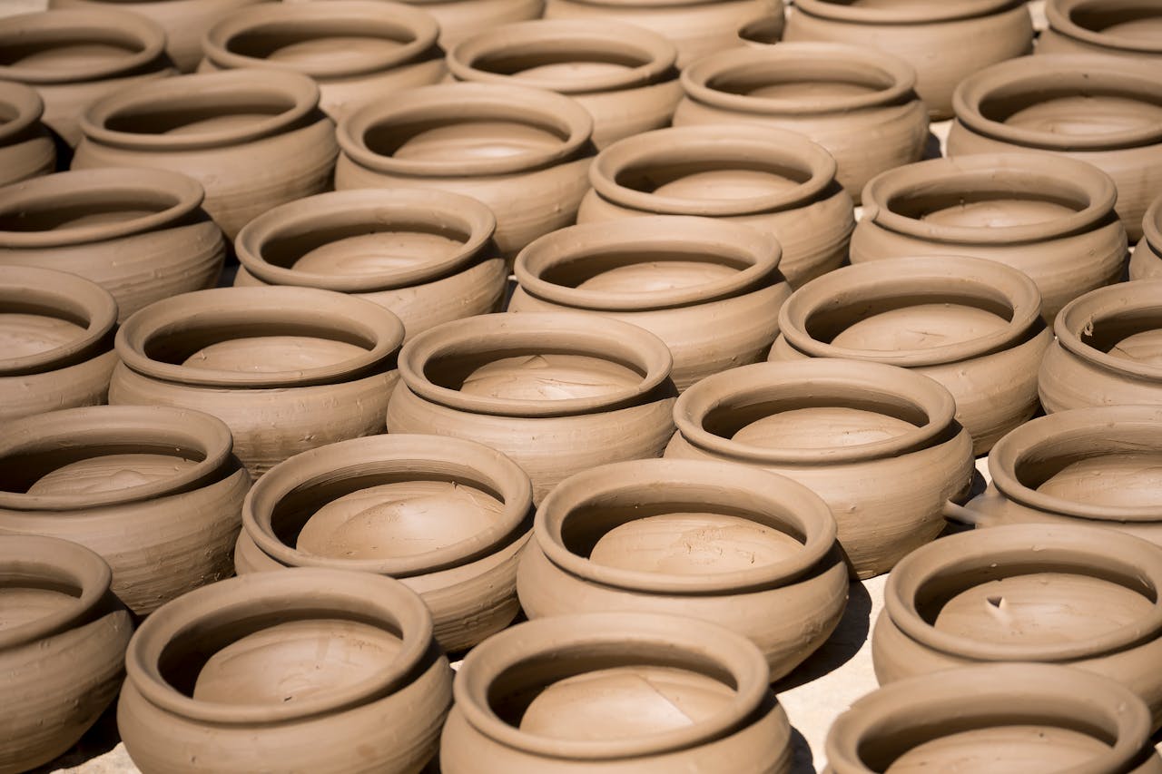 Rows of unfinished handmade clay pots drying in the sunlight, showcasing traditional pottery.