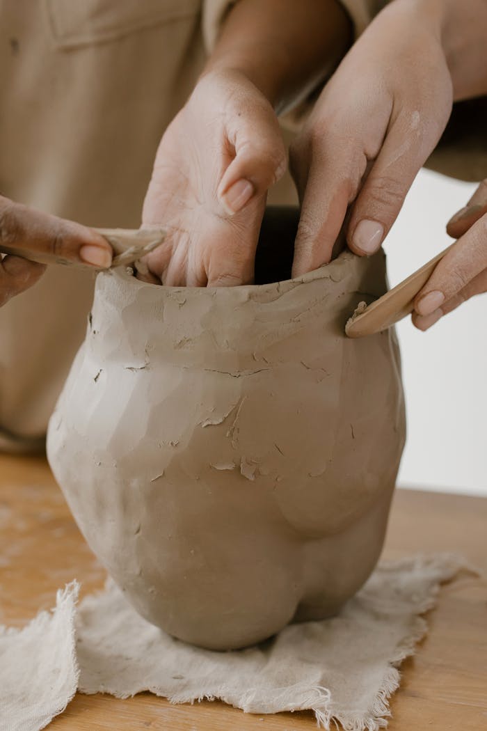 Detailed view of hands molding a clay pot in a pottery workshop, showcasing craftsmanship and creativity.