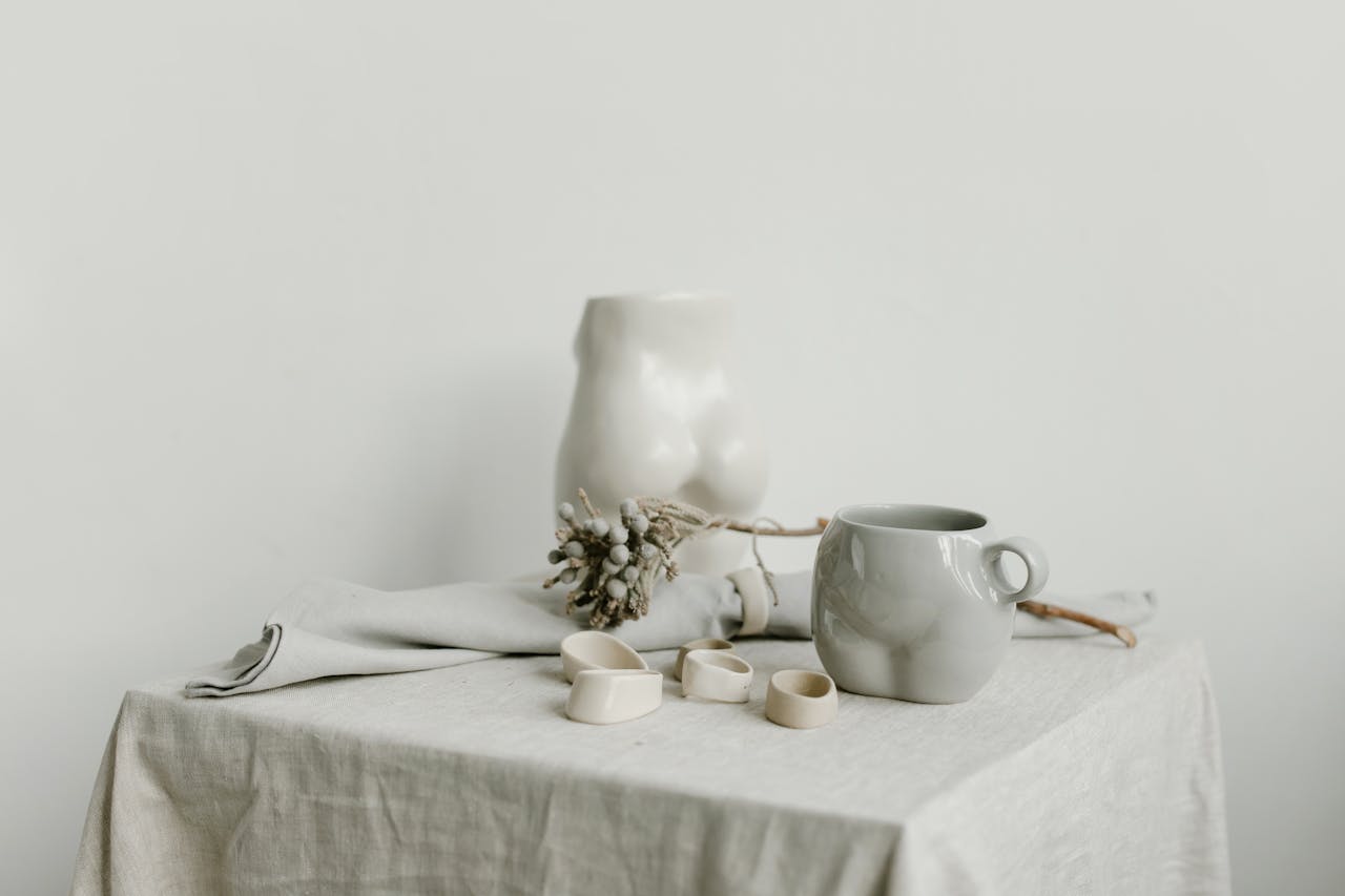 Elegant minimalist still life featuring a porcelain mug, ceramic sculpture, and soft linen drape.